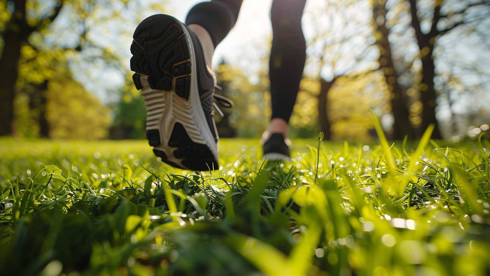 Ein Jogger läuft über eine grüne Wiese. Zu sehen sind nur die Füße mit Sportschuhen.